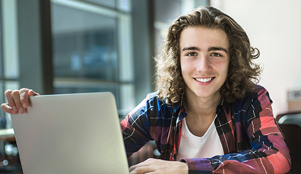 Young man smiling whilst working on his laptop.