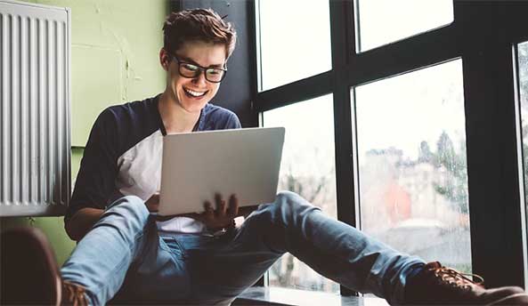 Young man sitting down and contently working on his laptop