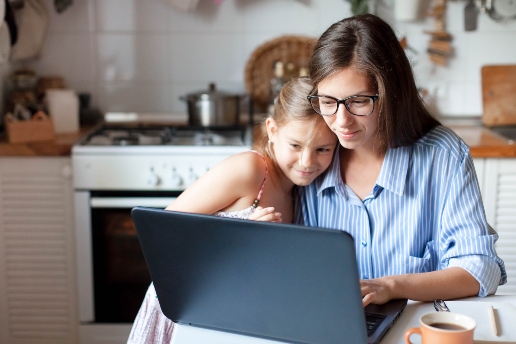 A mother and daughter embracing whilst enjoying time on their laptop