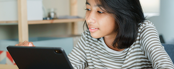 Young girl smiling at what she is watching on her iPad.