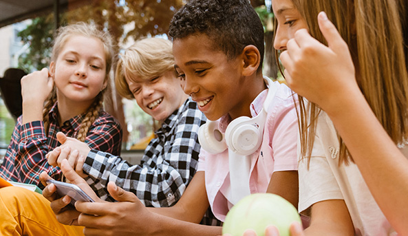 Group of four young friends smiling and laughing at what they are watching on a mobile phone