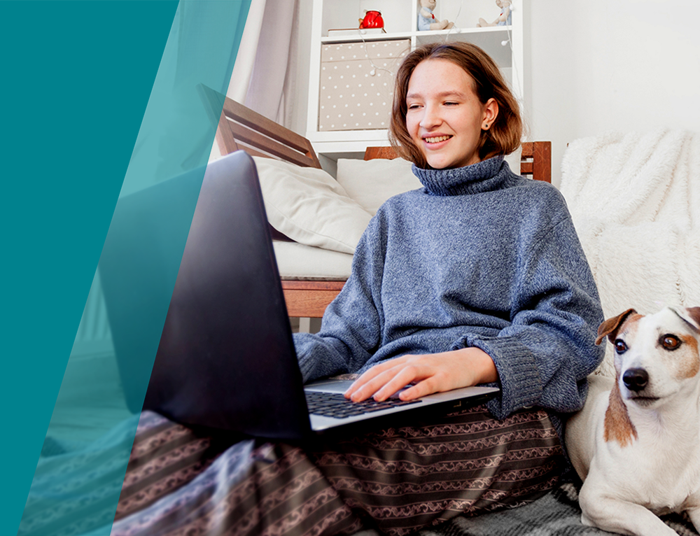 Young woman happily on her laptop whilst sitting down with her dog.