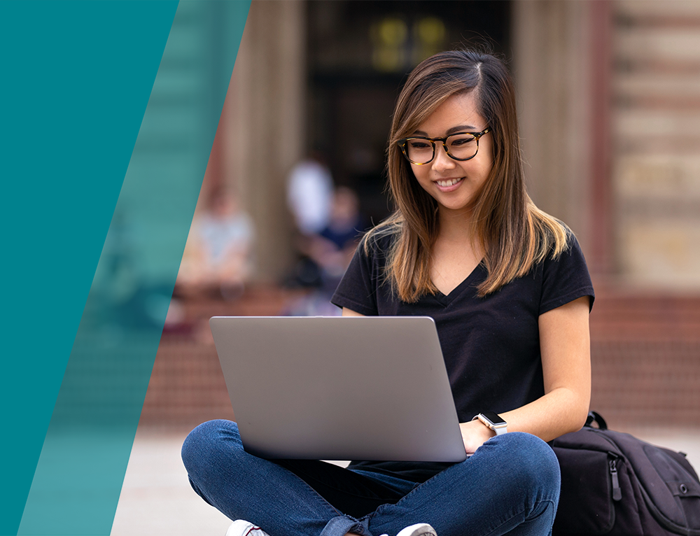 A young woman happily working on her laptop outdoors.