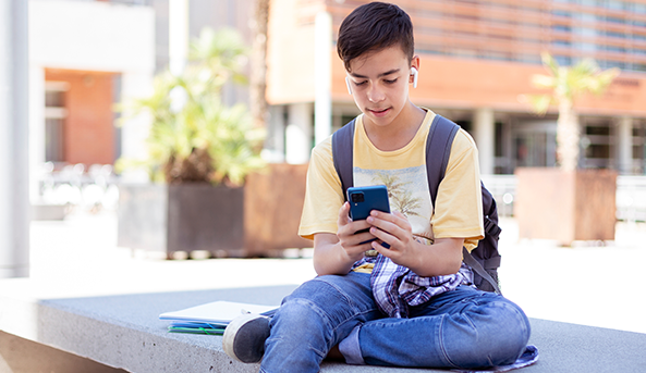 School boy playing on his mobile phone outdoors.