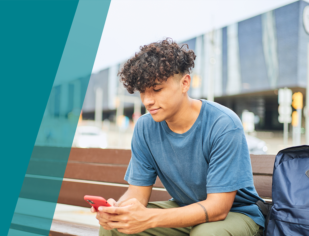 young boy sitting on a city bench talking on a mobile phone