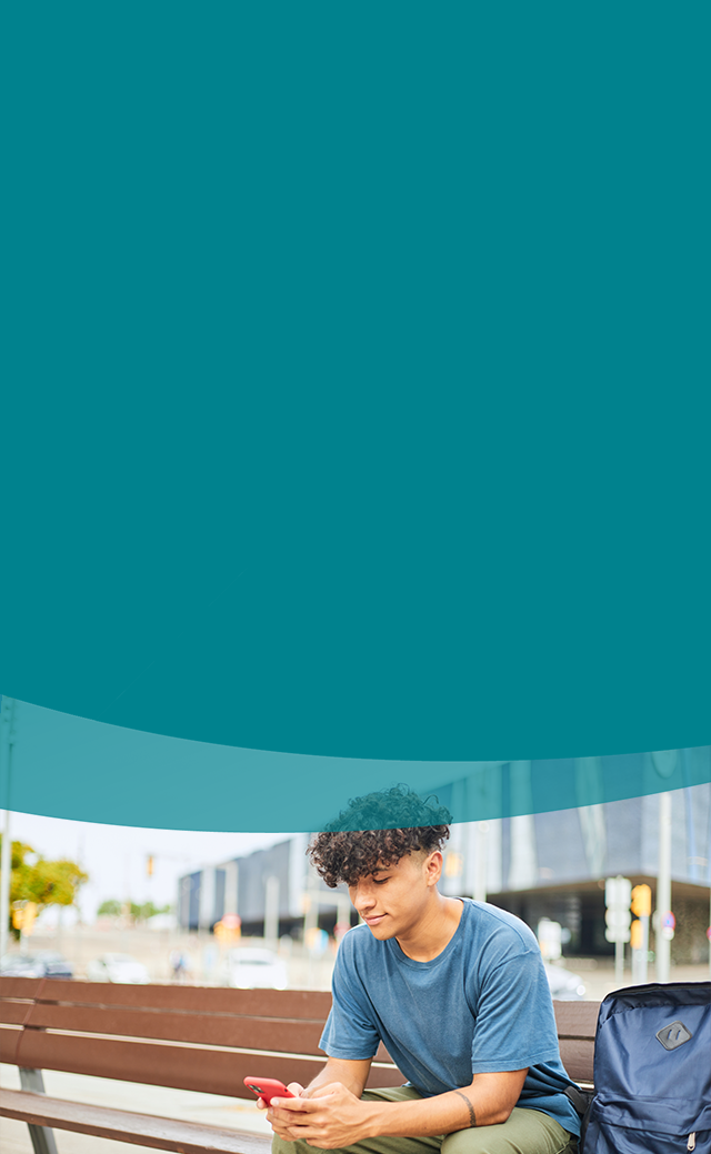 young boy sitting on a city bench talking on a mobile phone