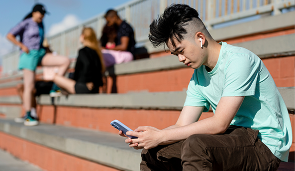 Teen boy using smartphone alone away from friends