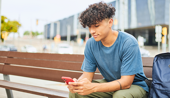 Young boy sitting on a city bench talking on a mobile phone