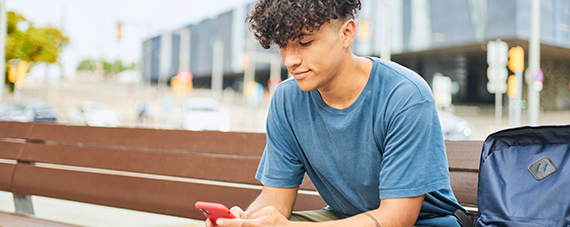 young boy sitting on a city bench talking on a mobile phone